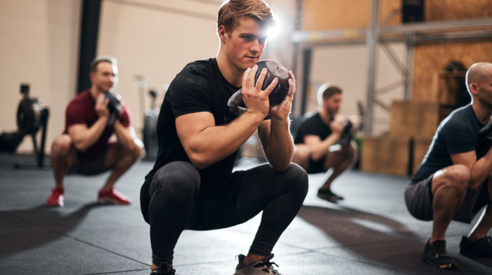 man squatting with weight in a group