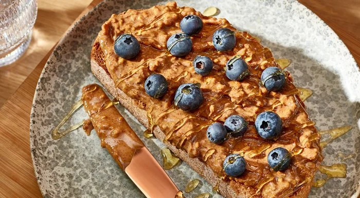 A nutritious pre-workout snack of wholegrain toast with peanut butter, topped with blueberries and a drizzle of honey.